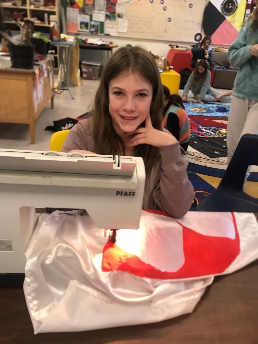 A child sitting at a table with a sewing machine
Description automatically generated