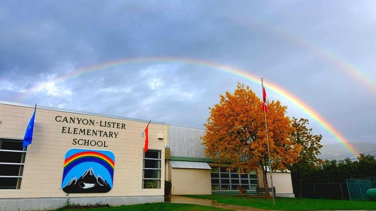 Canyon Lister Elementary School Elementary school with rainbow sign and double rainbow against billowy cloud-covered sky in background