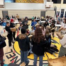 Staff and students drumming in a circle in a school gymnasium.